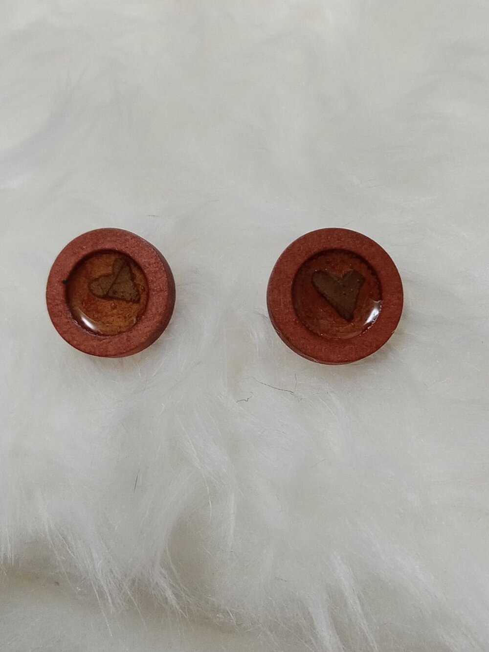 Handmade earrings on a wooden base with a piece of punched-out tree leaf